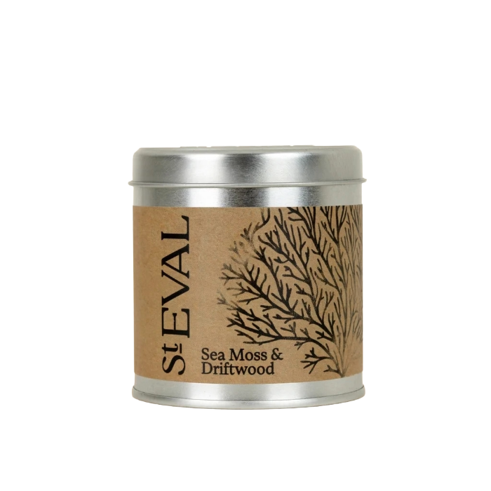 A St Eval Sea Moss & Driftwood scented candle in a round silver metal tin with a brown kraft paper label featuring a black branch illustration.