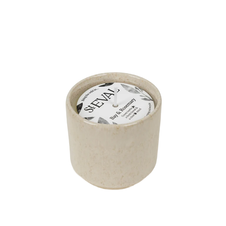 A small cylindrical candle in a speckled beige ceramic pot with a white wick and a round white label reading 'SAEVAL' and 'Rose & Rosemary'.