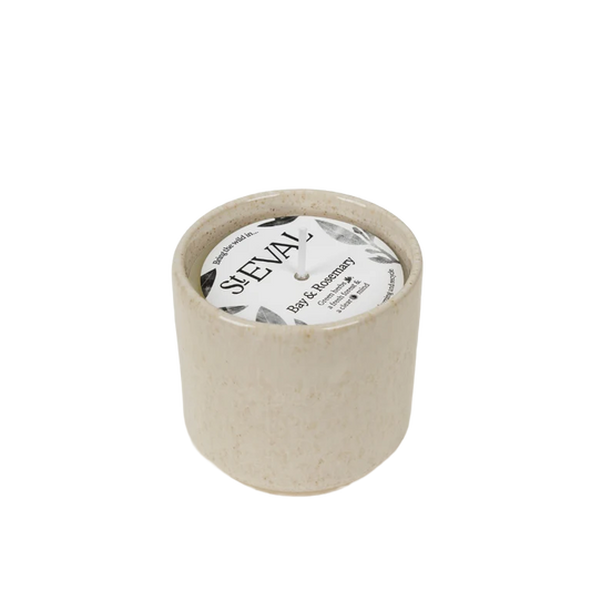 A small cylindrical candle in a speckled beige ceramic pot with a white wick and a round white label reading 'SAEVAL' and 'Rose & Rosemary'.