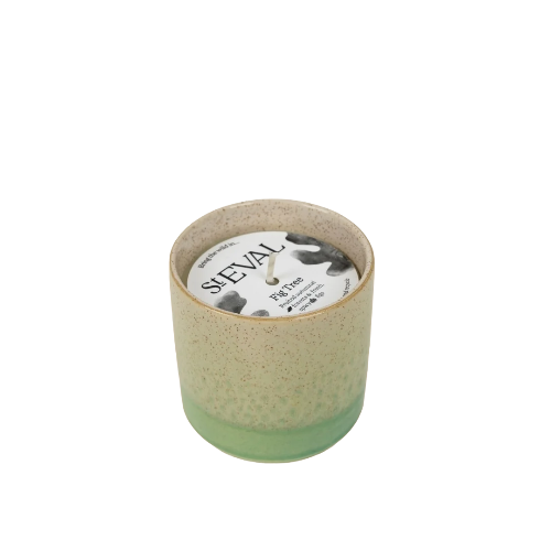 A ceramic candle in a speckled beige and light green pot with a cow-print lid, on a plain white background.