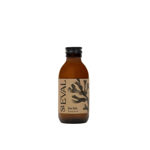 A small amber glass bottle of St Eval Sea Salt Scented Oil with a black cap and a beige label featuring a dark branch illustration, centered on a white background.