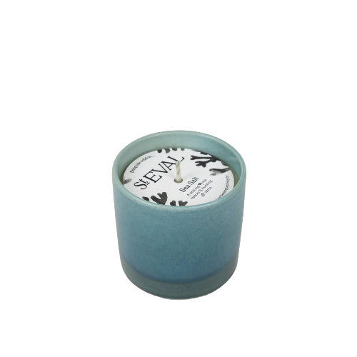A teal blue-green ceramic candle in a cylindrical holder with a white paper label that reads 'SHEVAL'.