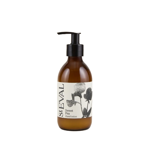 An amber glass pump bottle of SEVAL Sweet Pea Hand Lotion with a black pump and a cream label featuring black floral illustrations.
